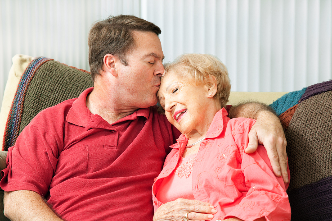 Son kissing mother’s forehead while sitting on the couch. 