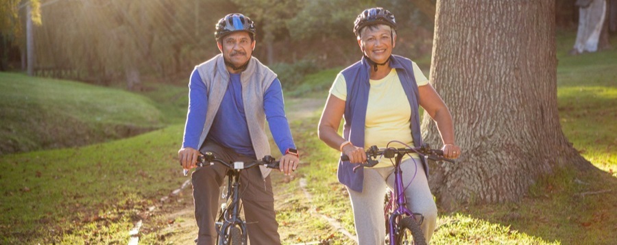 Two older adults riding their bikes in a park.