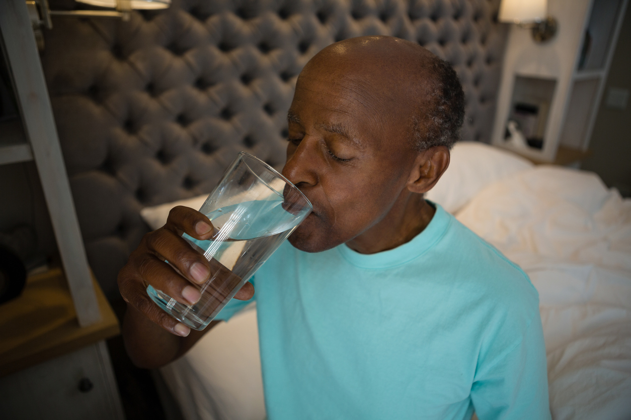 Older adult male in his room drinking water after swallowing his medication. 