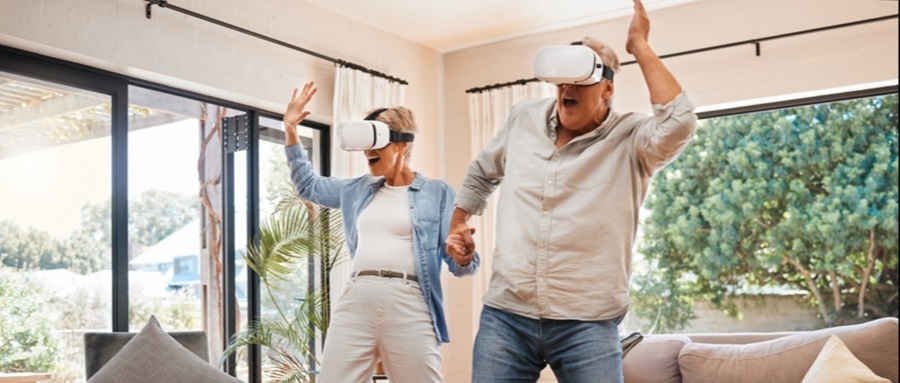 Two older adults holding hands and dancing with virtual reality headsets on.