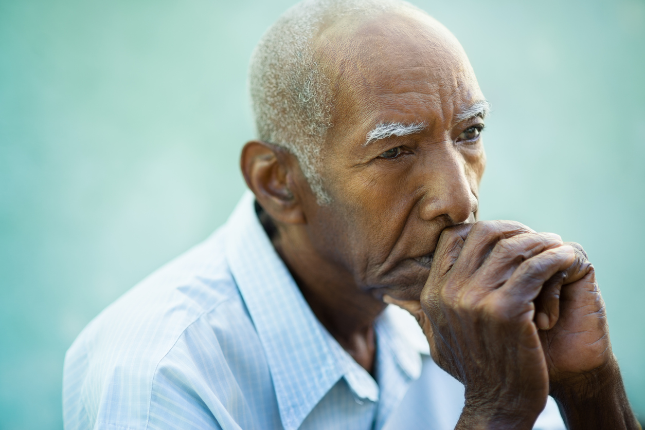 Male older adult staring into space with their hands on their mouth and chin. 