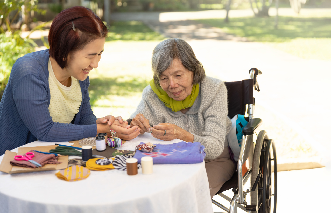 Wheelchair bound older adult female and her caregiver doing arts and crafts outside.  