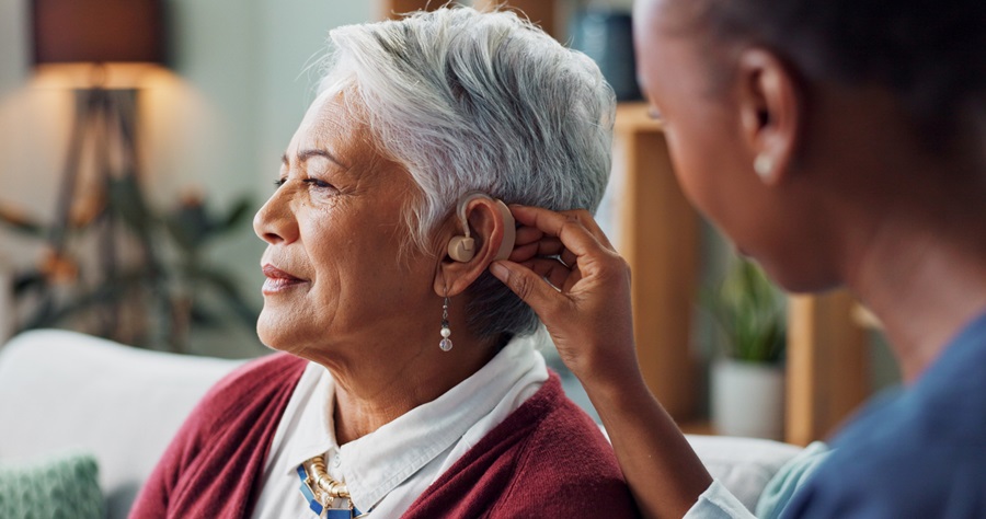 Elderly woman getting fitted with a hearing aid by a health professional.