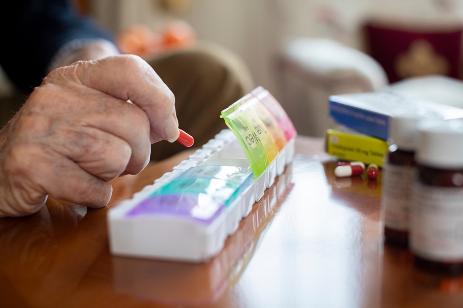Older adult organizing medication into pill box while several medication bottles and pills are on the table.