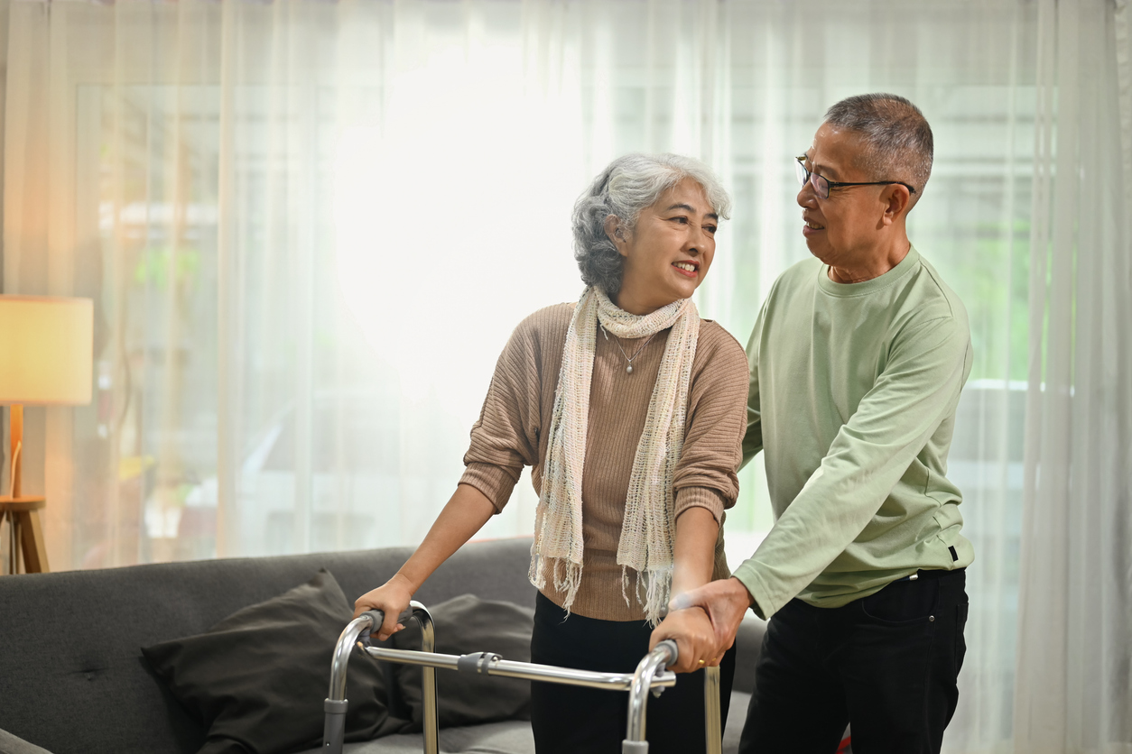 Woman with a walker standing up in a living room with a man helping behind her.