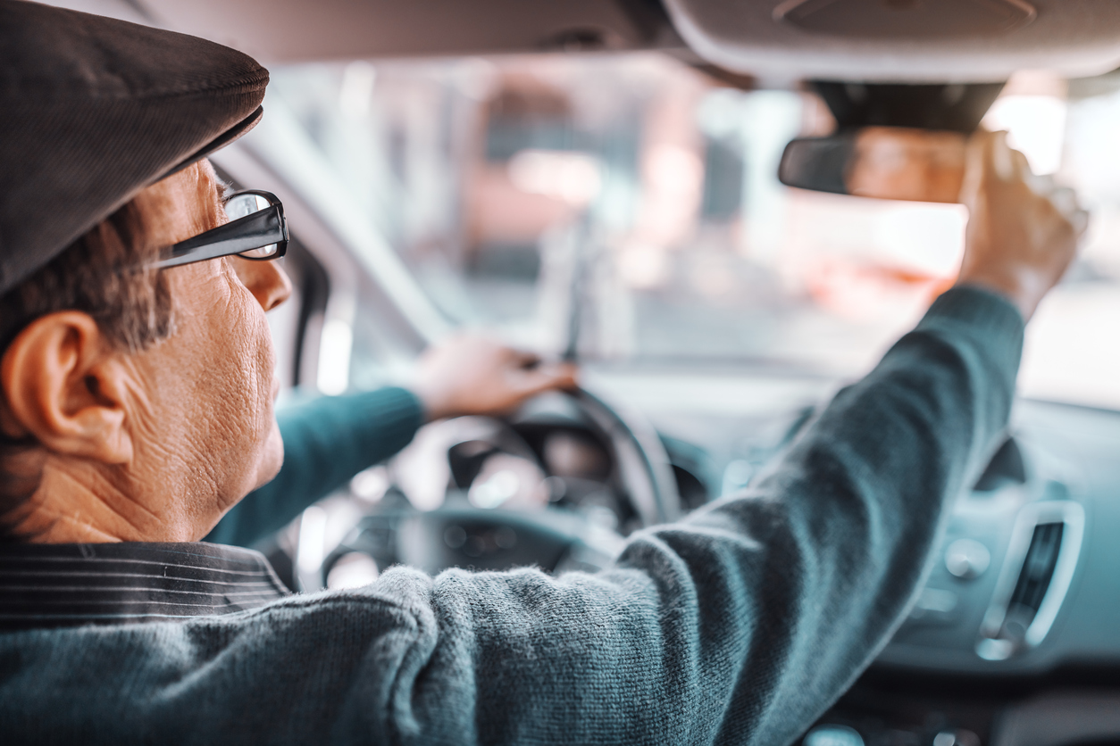 Older man driving car and adjusting mirror