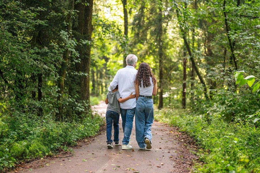 Older adult with teenager and young child walking along a path towards light