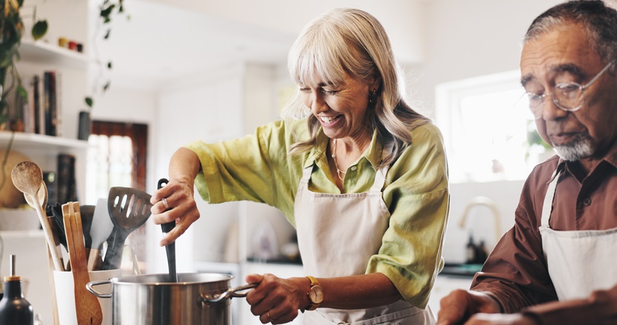Two older adults cooking; one stirring and the other chopping.