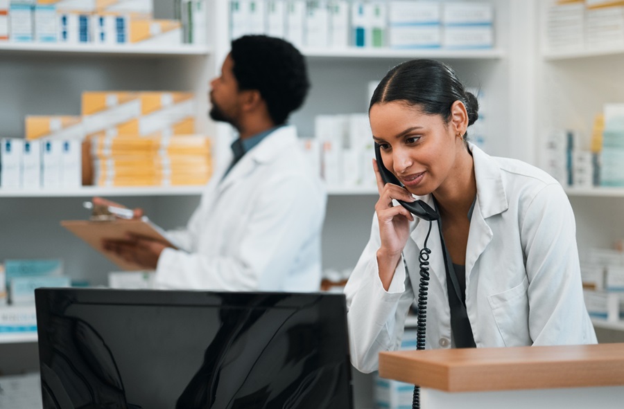 One pharmacist looking at inventory on a shelf while another pharmacist is on the phone.