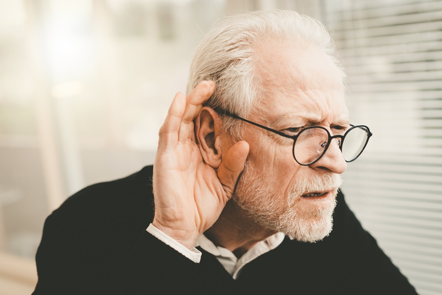 Elderly man having difficulty hearing and cupping his ear.