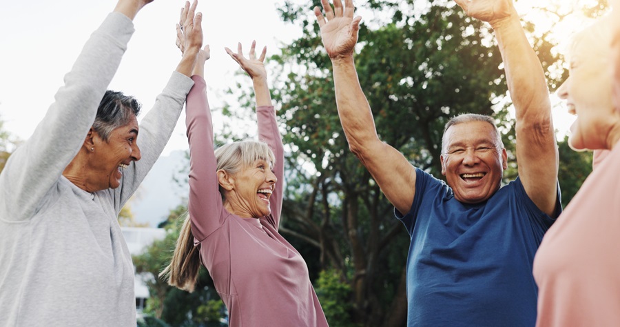 Group of older adults celebrating with their hands in the air and smiles while standing in a park.
