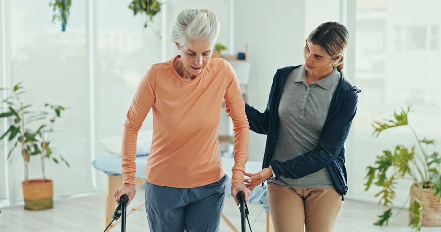 Older adult walking with with the assistance of a physiotherapist and a walking aid.