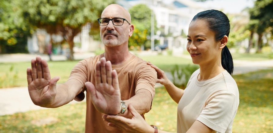 Man doing tai chi in a park with guidance from a teacher.